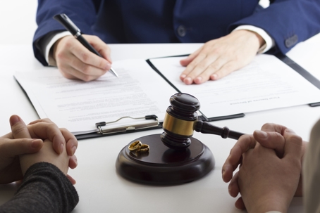 Close-up of a couple sitting across from a lawyer with divorce papers, a gavel, and wedding rings on the table. | Cascade Legal Services